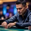 A man in a dark shirt and gold watch sits at a casino poker table, focused on arranging his chips—reminiscent of Phil Ivey’s intensity—with a blurred background of blue lights and other players.